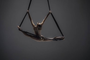 Modern koreografi ve akrobasi yaratıcı reklam konsepti. Kadın jimnastikçi monokrom stüdyosunda izole edilmiş. Akrobatik trapezdeki kız dansçı. Kayışları ikiye bölünmüş..