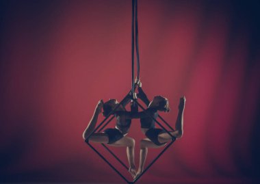 Modern koreografi ve akrobasi yaratıcı reklam konsepti. Kırmızı arka planda izole edilmiş kadın akrobatların portresi. Kız akrobatlar havada iplerle dönen dansçılar..