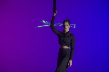 Genç akrobat elinde iple stüdyoda mor ışıkla poz veriyor. Siyah kostümlü jimnastikçi kız gösteri için hazırlan.