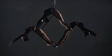 Bir küp üzerinde poz veren genç kadın akrobatların üçlüsü yüksekte asılı duruyor. Hava jimnastikçileri stüdyoda karanlık arka plana karşı performans sergiliyorlar ve esneklik ve esneklik gösteriyorlar. Sirk gösterisi konsepti