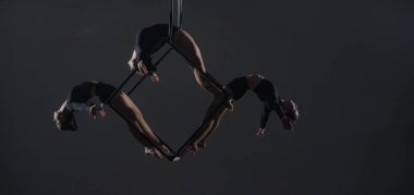 Bir küp üzerinde poz veren genç kadın akrobatların üçlüsü yüksekte asılı duruyor. Hava jimnastikçileri stüdyoda karanlık arka plana karşı performans sergiliyorlar ve esneklik ve esneklik gösteriyorlar. Sirk gösterisi konsepti