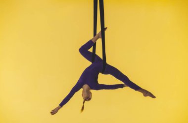 Modern koreografi ve akrobasi yaratıcı reklam konsepti. Sarı stüdyo arka planında izole edilmiş kadın jimnastikçi. Kız dansçı jimnastik kayışları üzerinde dönüyor, akrobatik öğeler gösteriyor..