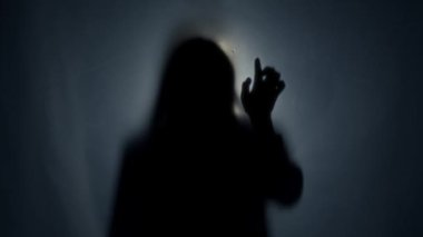 Paspas perdesinin arkasında, bir ışık demeti tarafından aydınlatılmış karanlık bir kadın silueti. Kadın işaret parmağıyla perdeye görünmez desenler çiziyor. Öbür dünya, öbür dünya.