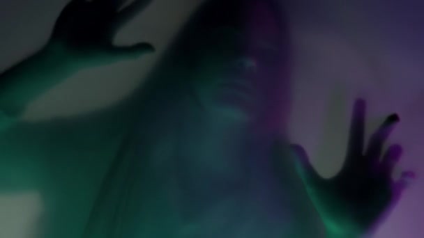 マットカーテンの背後にある女性の輝かしいシルエット ピンクと緑のネオンライトで 閉じます 女性が障壁に爪をかぶり それを引き裂こうとしています 幽霊と霊のコンセプト — ストック動画