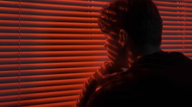 Siluet soyut yaratıcı reklam konsepti. Karanlık odadaki erkek portresi. Pencerenin yanında yakışıklı bir adam, kırmızı neon ışıkları külüstürün arkasında parlıyor, adam dışarı bakıyor, elleri havada..