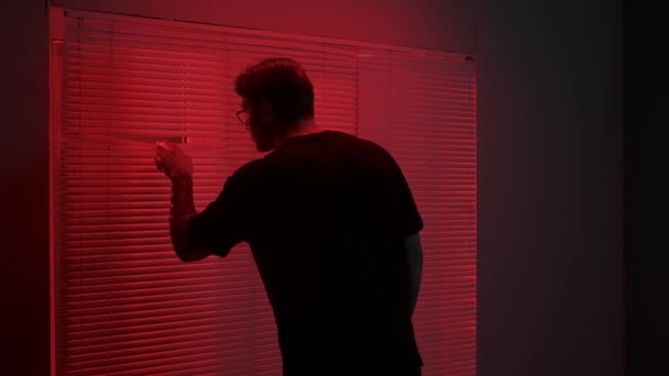 轮廓美学创意广告的概念 黑暗工作室里男模的肖像 戴眼镜的年轻人走到窗前 手中拿着红光 手拿着手把百叶窗打开 — 图库视频影像