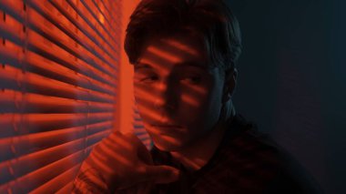 Siluet soyut yaratıcı reklam konsepti. Karanlık odadaki erkek portresi. Pencerenin yanında yakışıklı bir adam, kırmızı neon ışıkları külüstürün arkasında parlıyor, adam omzunun üstünden bakıyor, ifadesini dinliyor..