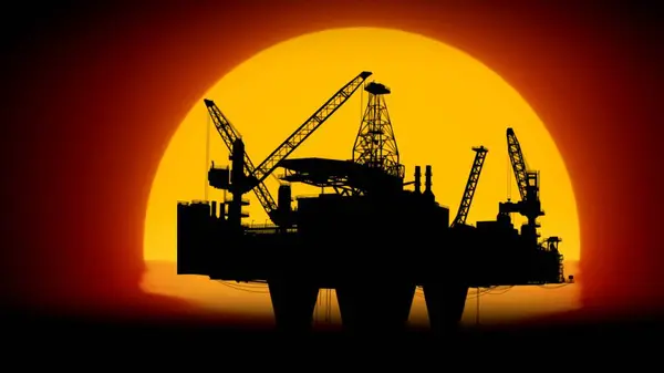 Modern technology of power industry creative advertisement concept. Shot of offshore oil platform in the sea against setting sun. Large drilling rig with towers extracting crude oil in the ocean.