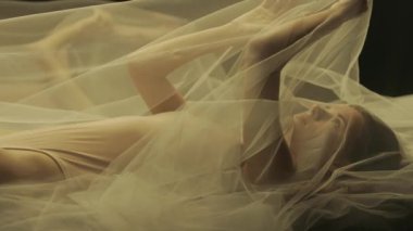 Yatakta, şeffaf bir hava bezinin altında genç bir kadının yan görüntüsü. Yaklaş. Sıcak ışıkla aydınlatılan bir kadın sıvı bir aynaya yansıtılır. Kadın nazikçe beyaz kumaşa dokunuyor.
