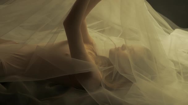 一个被白色网状郁金香覆盖的女人躺在黑色的背景上 光线反射在女人的皮肤上 风在她身上的织物上荡漾着涟漪 慢动作 — 图库视频影像