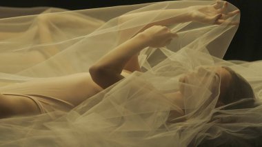 Yatakta, şeffaf bir hava bezinin altında genç bir kadının yan görüntüsü. Yaklaş. Ilık ışıkla aydınlatılmış bir kadın sıvı bir aynaya yansıtılır.