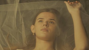 Şeffaf örgü tülle kaplı genç bir kadının üst görüntüsü, yakın çekim. Çekici bir kadının portresi Ilık ışıkla aydınlatılmış