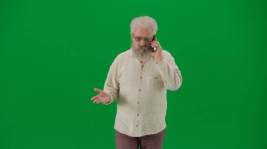 Emekli eğlencesi ve günlük yaratıcı reklam konsepti. Krom anahtar yeşil ekranda yaşlı sakallı adamın portresi. Kıdemli adam kameraya bakıyor, akıllı telefondan konuşuyor.