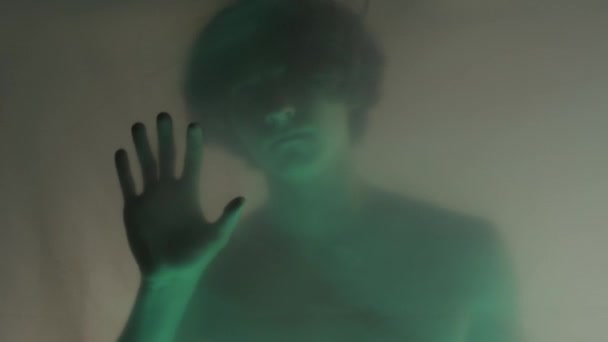 マットカーテンの後ろに 緑のネオンライトの 裸のトーソの輝かしいシルエットを 閉じます 男はそれを引き裂こうとして 障壁に指の爪をかぶっている 幽霊の概念と — ストック動画