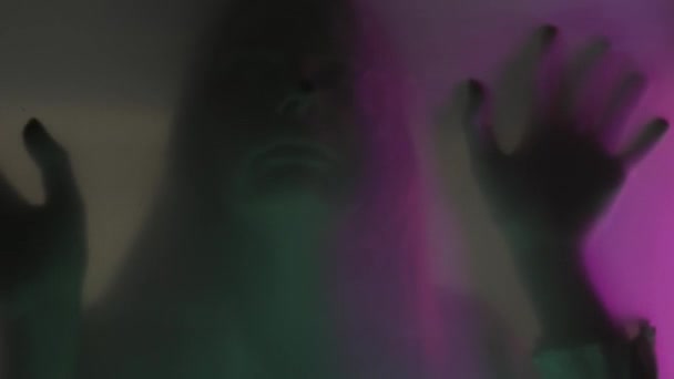 在粉色和绿色的霓虹灯下 一个女人在垫子幕后面的模糊的轮廓被关闭了 女人碰了碰透明的屏障 双手从绝望中垂下 鬼怪的概念和 — 图库视频影像