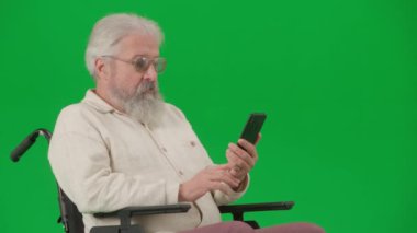Emeklilerin bakımı ve günlük yaratıcı reklam konsepti. Krom anahtar yeşil ekranda sakat bir adamın portresi. Tekerlekli sandalyedeki son sınıf öğrencisi akıllı telefondan video konuşması yapıyor..