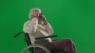 Emeklilerin bakımı ve günlük yaratıcı reklam konsepti. Krom anahtar yeşil ekranda sakat bir adamın portresi. Tekerlekli sandalyedeki son sınıf öğrencisi eski film kamerasıyla fotoğraf çekiyor..