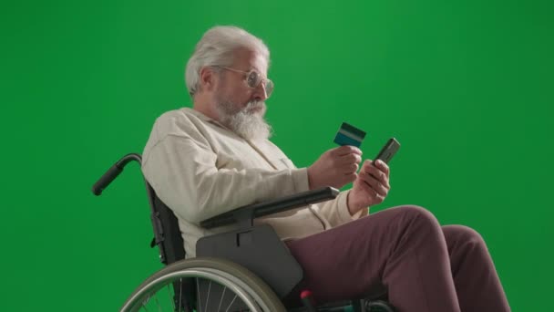年金受給と日常生活クリエイティブ広告コンセプト クロマ グリーン スクリーンの老化した障害者の肖像画 スマートフォンでカード番号を入力する車椅子のシニアマンを閉じる — ストック動画