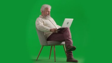 Emekli eğlencesi ve günlük yaratıcı reklam konsepti. Krom anahtar yeşil ekranda yaşlı sakallı adamın portresi. Son sınıf öğrencisi sandalyede oturmuş bilgisayardaki video görüşmesiyle sohbet ediyor..