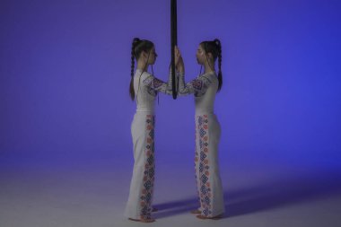 Modern koreografi ve akrobasi yaratıcı reklam konsepti. Kadın jimnastikçiler mor neon stüdyosunda izole edilmiş. Kızlar ikilisi havada kayışlarla ringde dans ediyor..