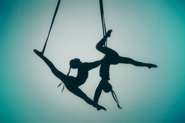 Modern koreografi ve akrobatik yaratıcı konsept. Ortasında spot ışığı olan mavi bir arka planda iki kadın akrobatın silueti. Dişi akrobatlar ipler üzerinde akrobatik elementler sergiler.