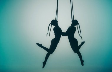 Modern koreografi ve akrobatik yaratıcı konsept. Ortasında spot ışığı olan mavi bir arka planda iki kadın akrobatın silueti. Dişi akrobatlar ipler üzerinde akrobatik elementler sergiler.