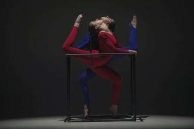 Modern koreografi ve akrobasi yaratıcı reklam konsepti. Siyah arka planda izole edilmiş iki kadın akrobatın portresi. Mavi takım elbiseli kızlar bir küpte element gösteriyorlar..