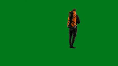 Sırtında büyük bir sırt çantası olan bir erkek gezginin arka görüntüsü. Adam tam yol ayakta ve manzaranın tadını çıkarıyor. Stüdyoda yürüyen yeşil ekranda