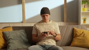 Müzik ve insan duyguları yaratıcı reklam konsepti. Odada kanepede oturan bir gencin portresi. Kulaklıklı adam akıllı telefondan müzik dinliyor, kafasıyla ritim tutuyor..