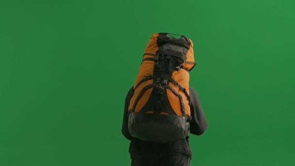 緑色のスクリーンに重いバックパックで歩く疲れたハイカーのバックビュー 男は手で額から汗を拭く アウトドアアドベンチャー 疲労のコンセプト — ストック動画