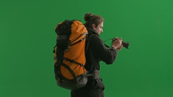 在远足过程中 一位男性旅行者用相机拍照的背景图 男子徒步旅行者在工作室的绿色屏幕上走近 积极休息 远足的概念 — 图库视频影像