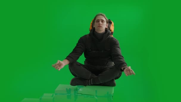 男性の旅行者は 丘の上にたくさんの姿勢で座って瞑想しています 背中のバックパックを持った男が緑色のスクリーンのスタジオで瞑想 — ストック動画
