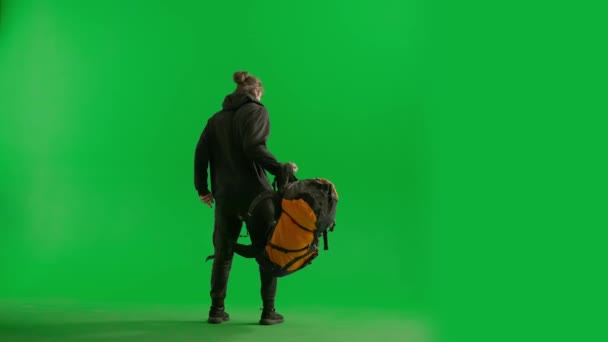 一个男性旅行者从背后从绿色屏幕上的工作室里取出背包的后视镜 这个人背着背包徒步旅行了很长时间 现在正弯弯曲曲 揉捏着疲倦的肌肉 — 图库视频影像