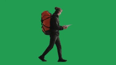 Bir erkek turist yürüyüş yaparken bölgenin haritasını inceler. Sırtında sırt çantası olan bir adam yeşil ekranda stüdyoda yürüyor.