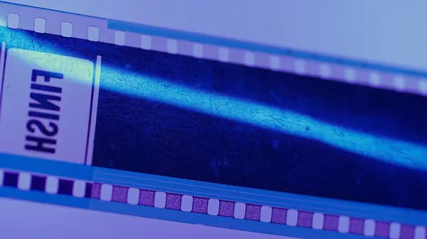 A scratched strip of photographic film labeled Finish on a pink background in blue neon light close up