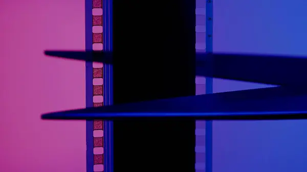 Scissors cuts a strip of photographic film on a blue and pink background close up