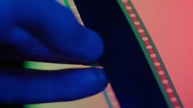 Negatif bir film şeridini gözden geçiriyorum. Filmin üzerinde mavi, yeşil ve kırmızı neon ışıklarla yürüyen erkeklerin parmakları.