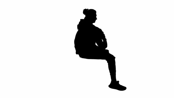 白い背景の上に座っている男性旅行者の黒いシルエット 男は彼の足でぶら下がって座り 彼の目に手を置き 遠くを見つめている サイドビュー — ストック動画
