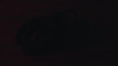 Karanlıkta, ahşap bir masanın üzerinde eski 35 mm film negatifleri şeklinde bükülmüş. Film ruloları kırmızı neon ışıkla aydınlatılır.