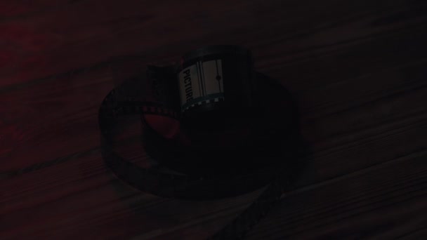 在黑暗的近处 被塞进一张木制桌子上成卷的35毫米胶片底片里 胶卷被红色的霓虹灯照亮了 — 图库视频影像