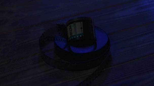 35Mmの古いフィルムのネガティブなロールを 暗闇に閉じ込められた木製のテーブルに巻き込んだ ブルーライトで照らされた映画のロールスロイス — ストック動画