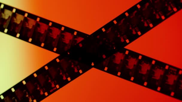 赤いオレンジ色の勾配の背景の写真フィルムの2つの交差したストリップが閉じます 赤いオレンジ色の光で牛を示す露出されたネガティブ — ストック動画