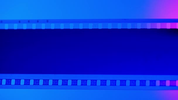 Порожня Нерозвинена Смуга Плівки Синьому Фоні Освітлена Рожевим Неоновим Світлом — стокове відео