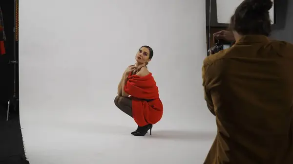 摄影制作和创造性团队合作的概念 工作室的模特和专业团队的后台 身着红色衣服的女模特坐在膝盖上拍照 — 图库照片