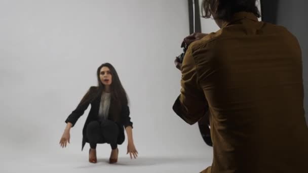 フォトショットとチームワーク バックステージ広告クリエイティブコンセプト スタジオのモデルと制作チーム スタジオで写真家のために床にポーズするスーツの魅力的なブルネット女性 — ストック動画
