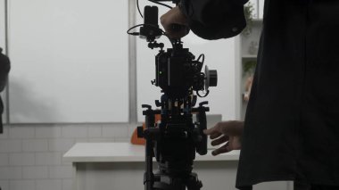 Ekip stüdyoda çekim için hazırlanıyor. Kameraman kamerayı bir tripoda monte eder.