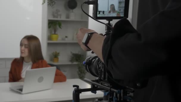 Відеооператор Налаштовує Камеру Збільшуючи Ведучому Сидячи Столом Перед Ноутбуком Жінка — стокове відео