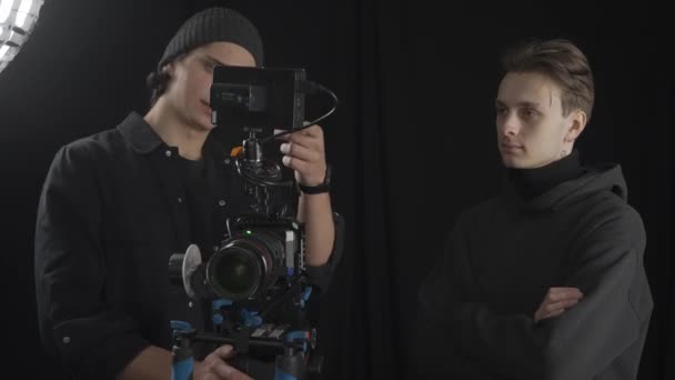 男摄影师和助手站在专业摄像机旁边 仔细阅读图片 男子讨论射击的构成 并为即将到来的射击准备设备 — 图库视频影像