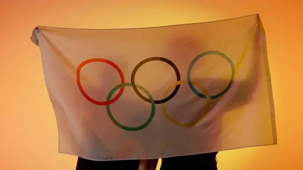 Sports flags advertisement concept. Silhouettes of people holding large flag with five rings on yellow background. Silhouettes of man and woman holding national flag with Olympic logo in hands.