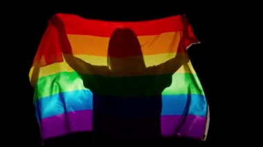Aşk ve çeşitlilik reklam kavramı. Siyah arka planda gökkuşağı bayrağı tutan kişi. LGBT gurur bayrağı tutan bir kadın silueti.